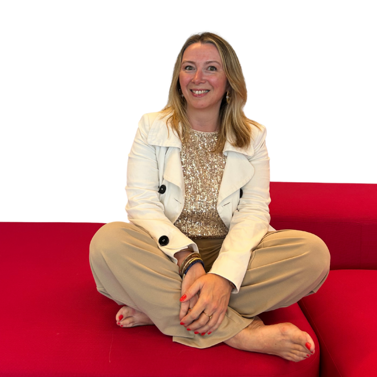 Tiphaine legaud votre analyste en Human Design Femme souriante assise en tailleur sur un canapé rouge, portant un pull beige et une veste blanche.